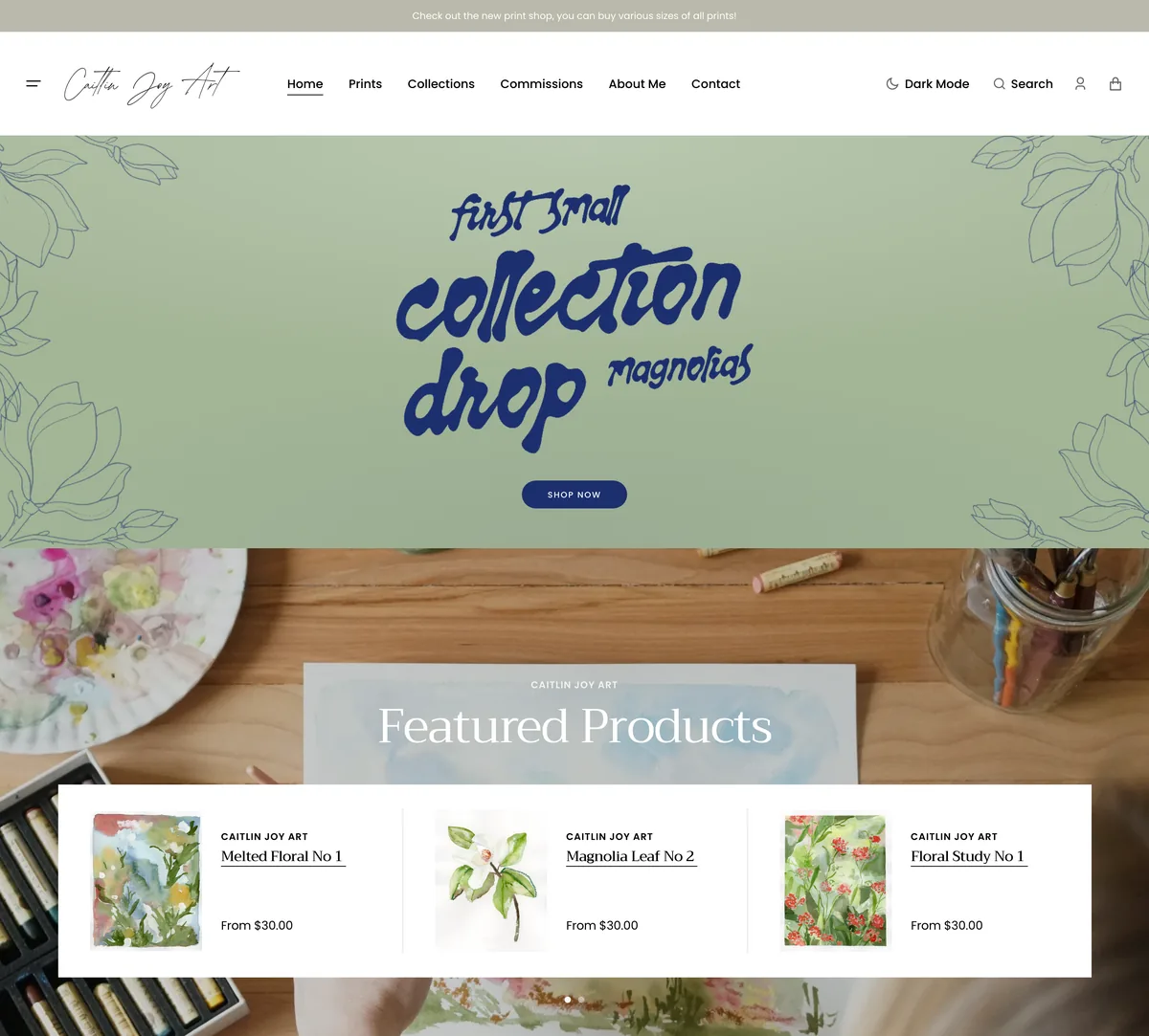 The Caitlin Joy Art homepage on desktop: the magnolias collection-drop hero on sage green above a featured products carousel.